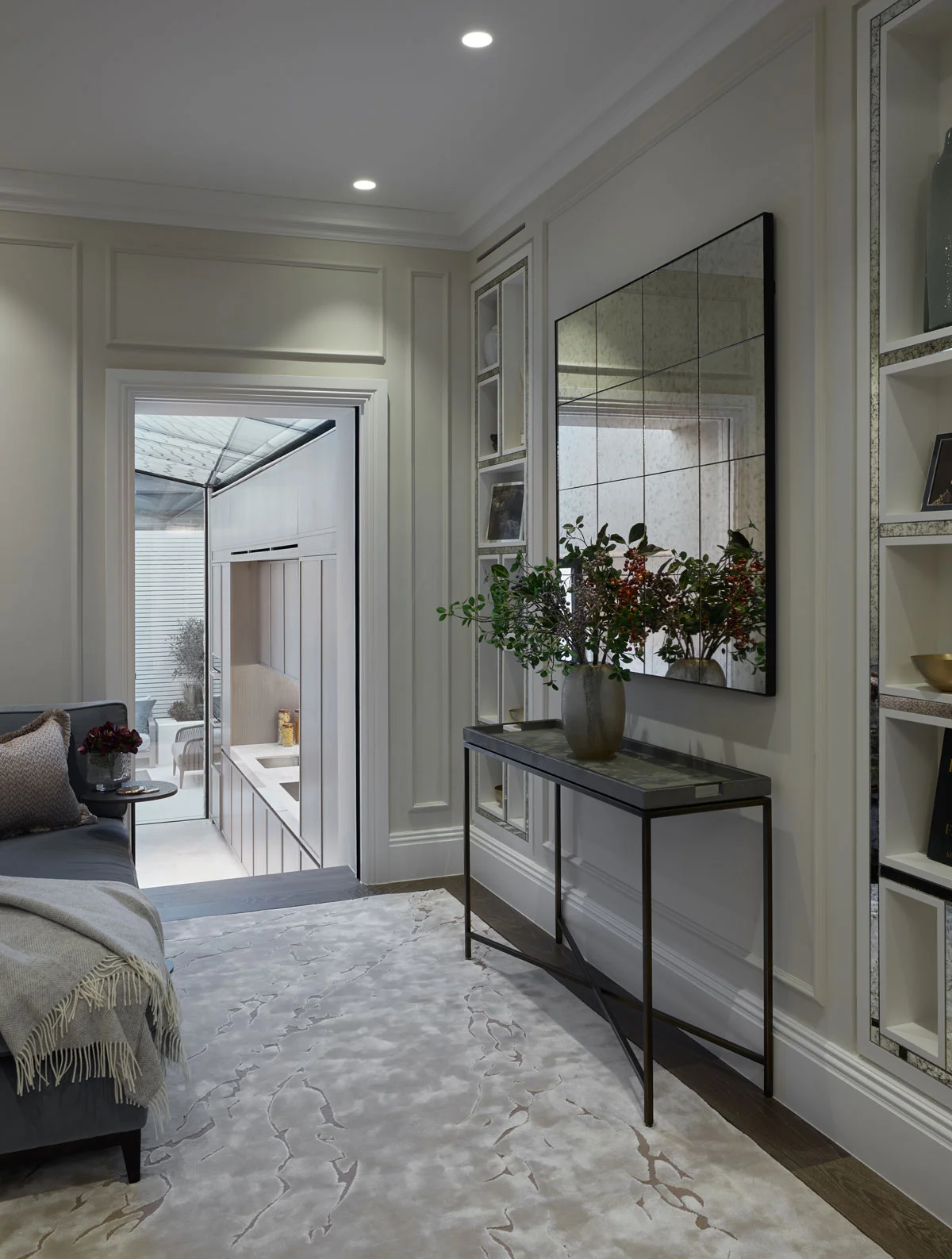 Modern interior featuring a stylish console table with a vase of flowers, soft rug, and a large mirror against the wall.