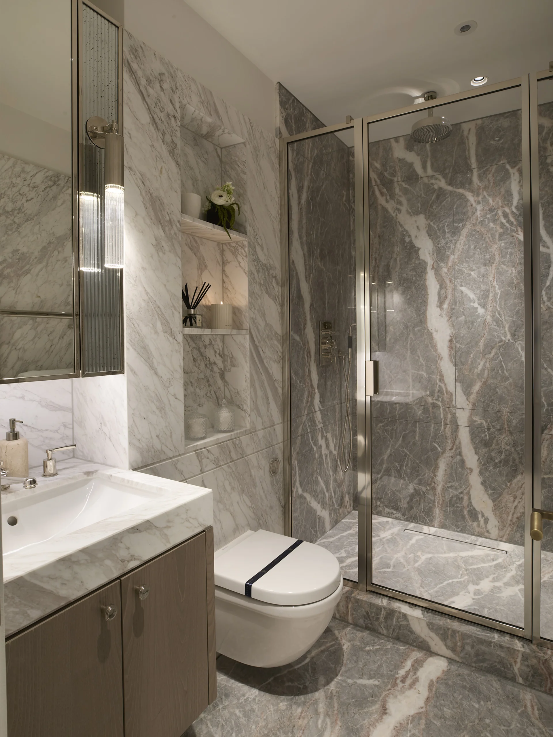 Modern bathroom featuring marble walls, glass shower, sleek vanity, and a contemporary toilet design.