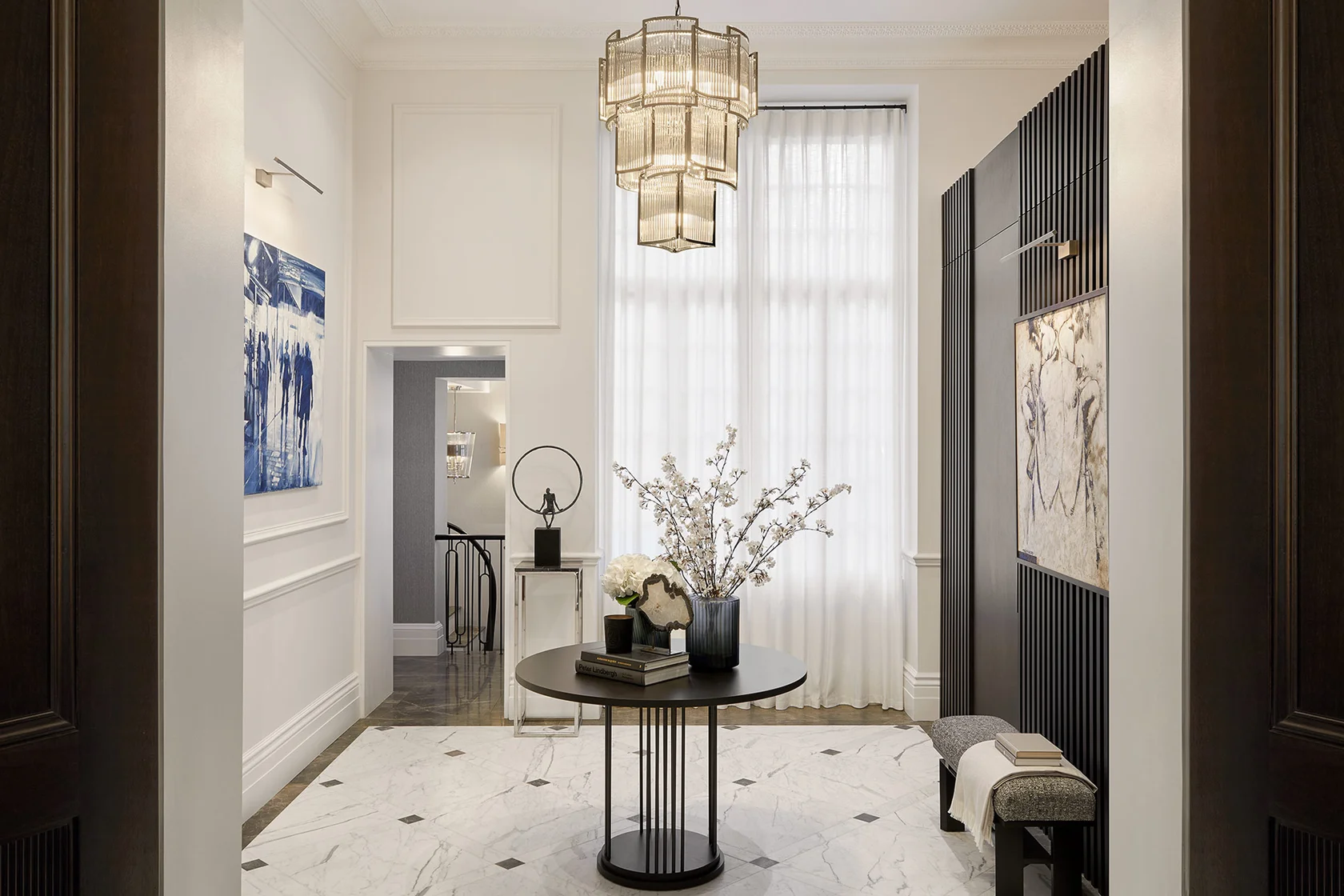 Bright hallway with sculptural pendant lighting, marble flooring, and curated artwork.