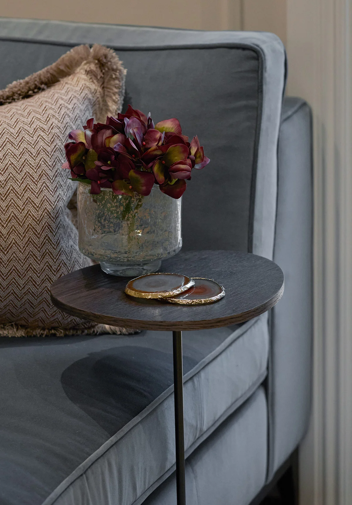 Living room side table styled with ceramic vase, floral arrangement, and textured cushions.