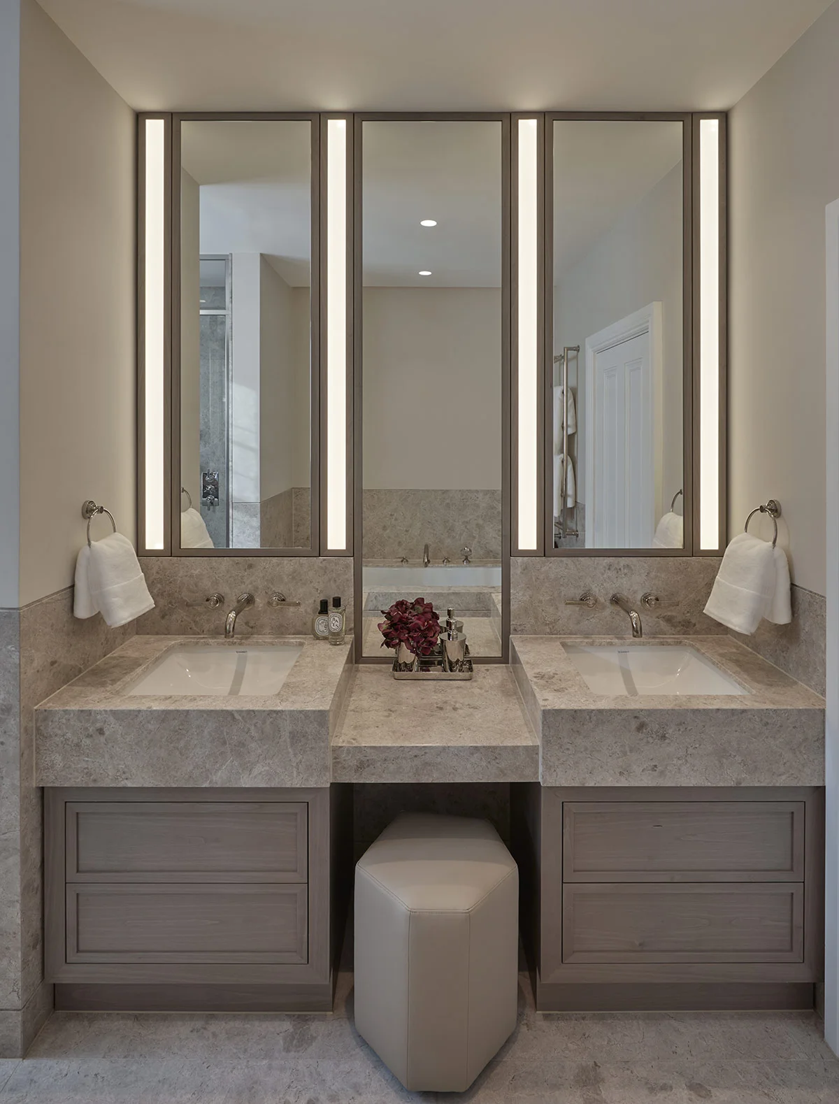 Double vanity bathroom with stone worktops, integrated basins, illuminated mirrored cabinets, and bespoke joinery.