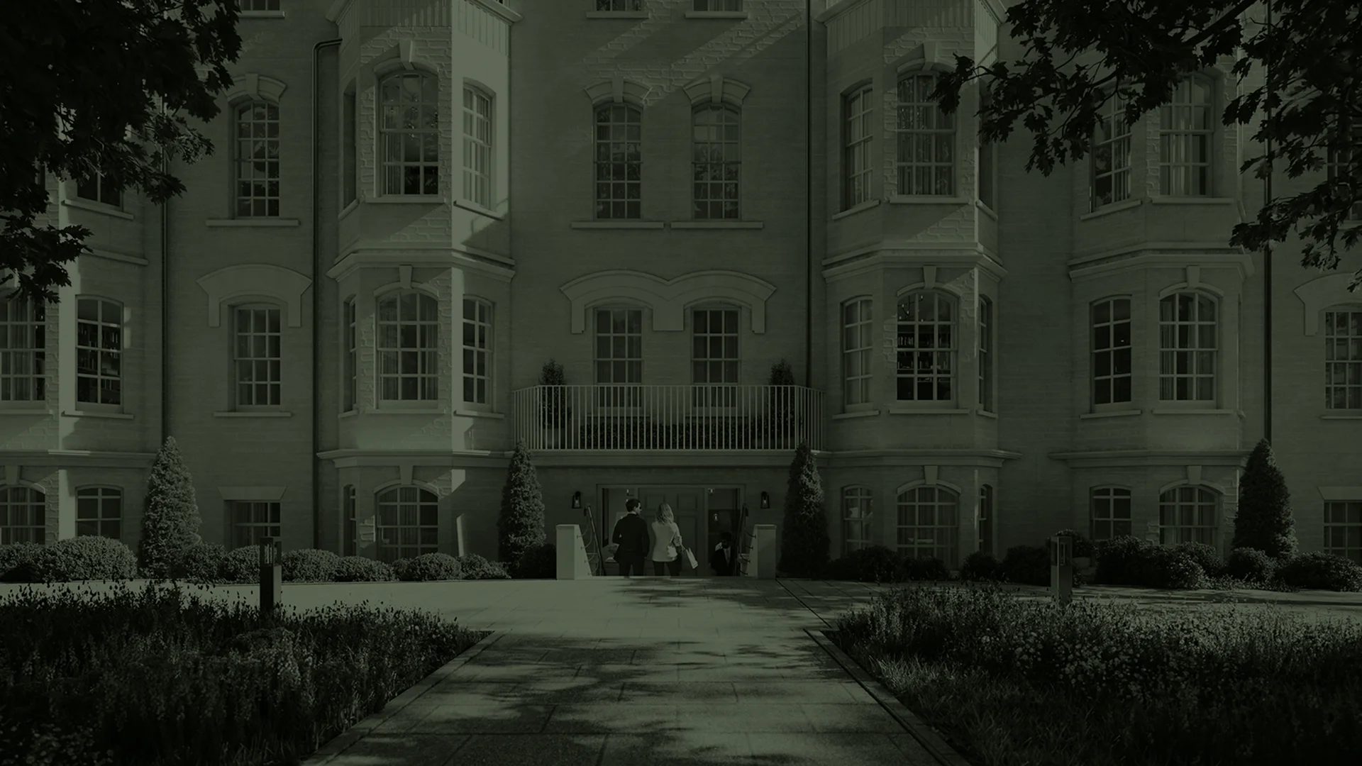 Elegant building entrance with people walking towards the door, surrounded by lush greenery and well-maintained landscaping.