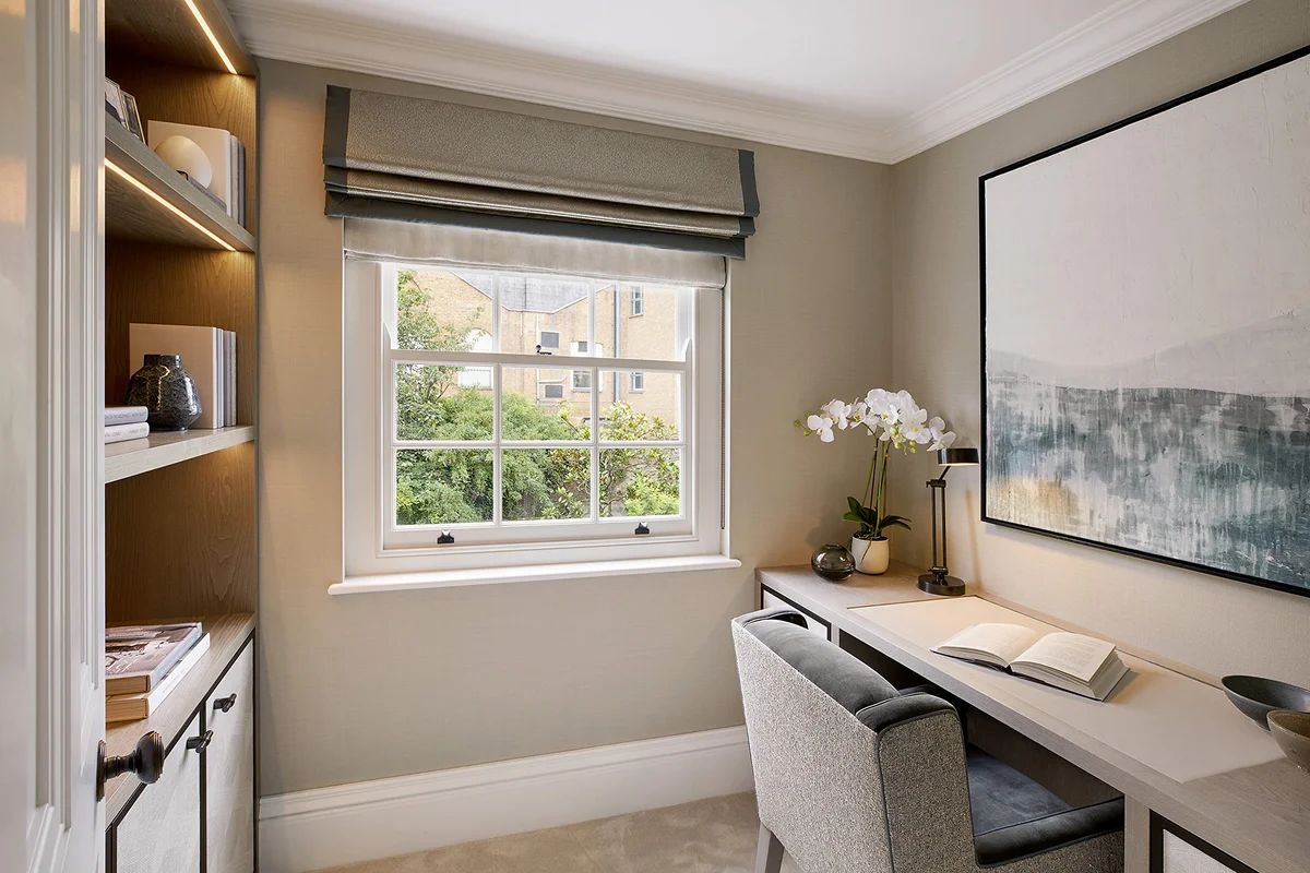 Cozy home office with a desk, chair, and artwork, featuring a window with a view of greenery.
