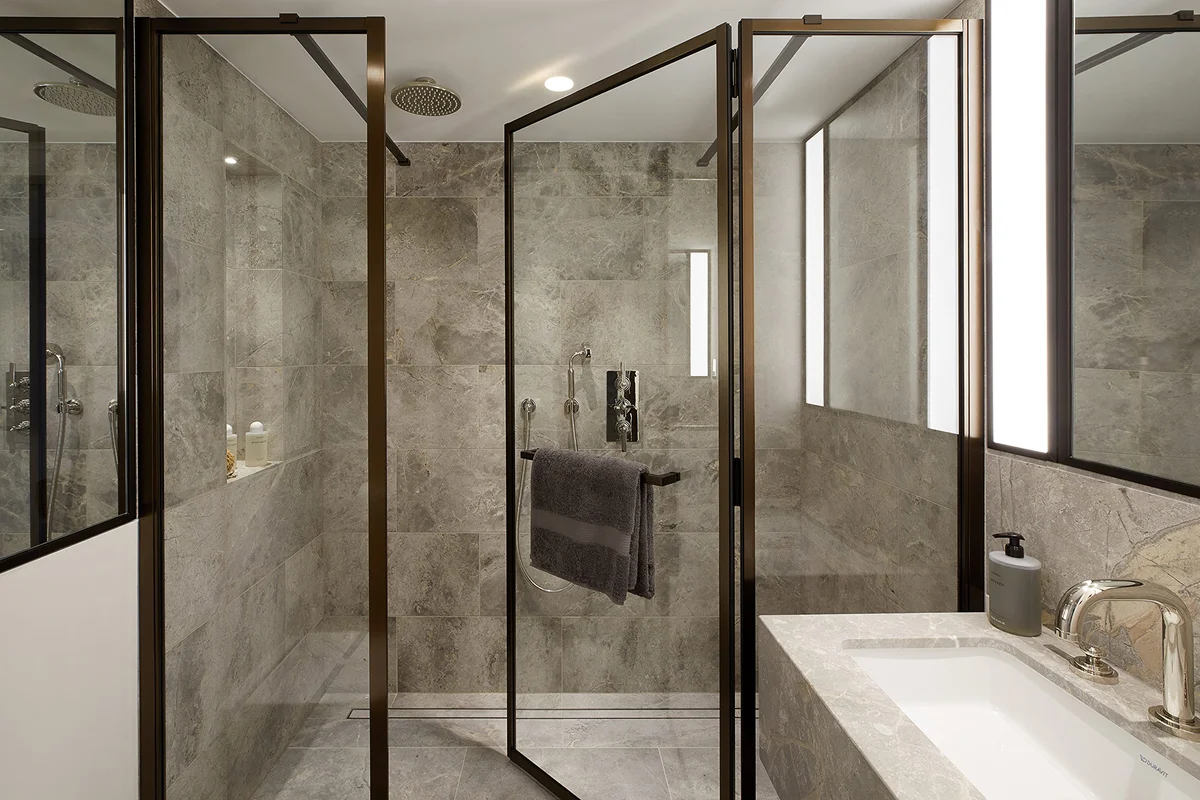 Modern bathroom featuring glass shower doors, marble walls, and a sleek sink with a large mirror.
