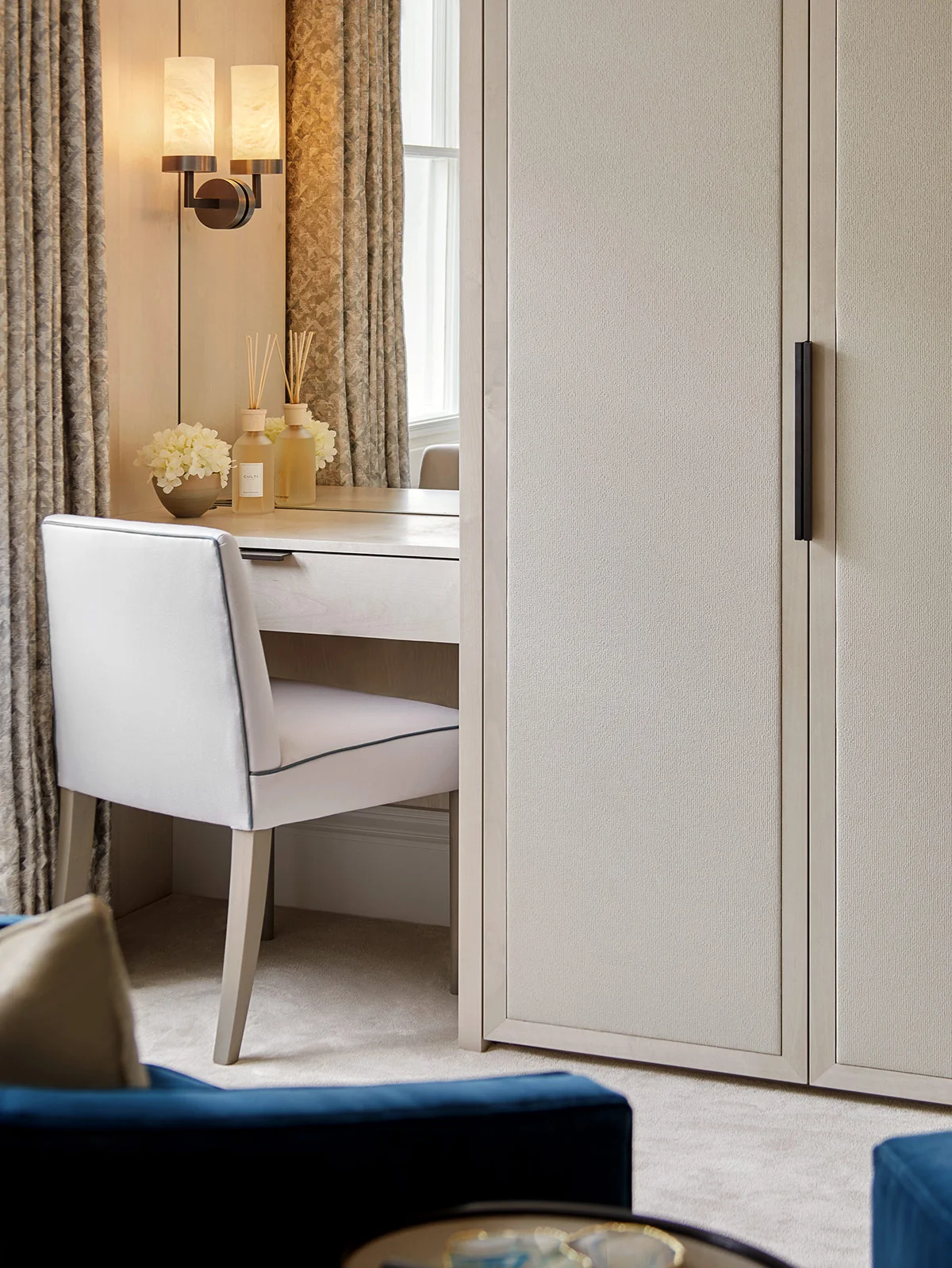 Elegant dressing area featuring a white chair and desk, accented by soft lighting and draped curtains.