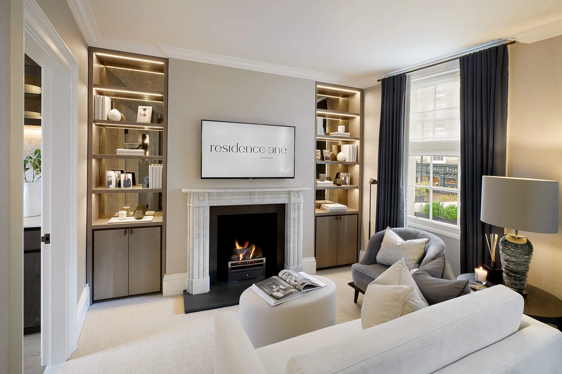 Modern living room featuring a fireplace, bookshelves, and large windows with stylish furnishings.