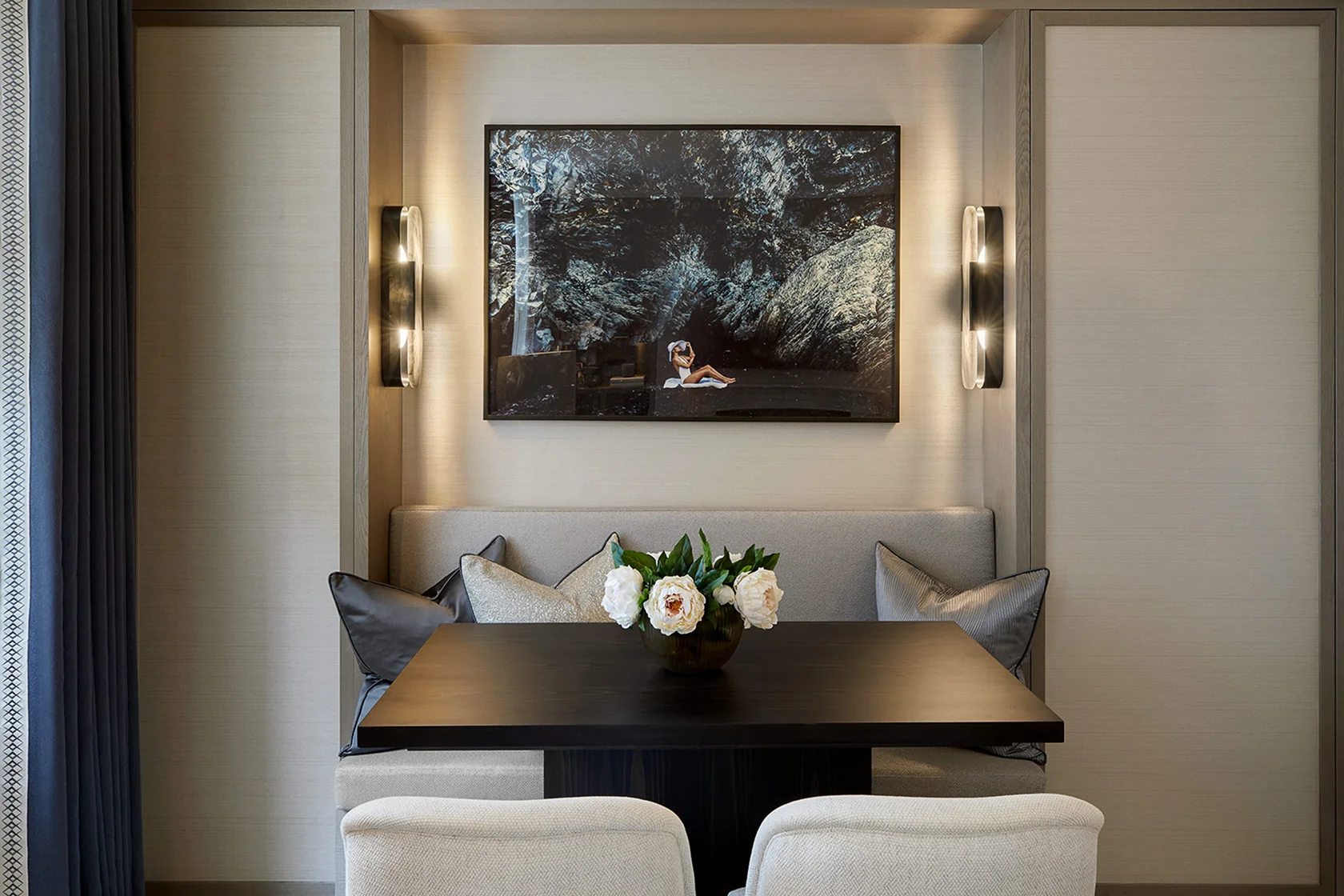 Dining nook with a black table, white chairs, and a floral centerpiece, framed by soft lighting and artwork on the wall.