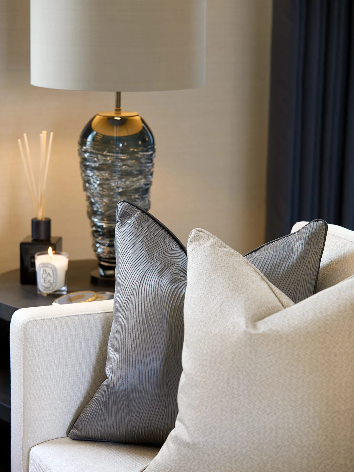 Decorative pillows on a white sofa beside a blue glass lamp and a candle on a dark table.