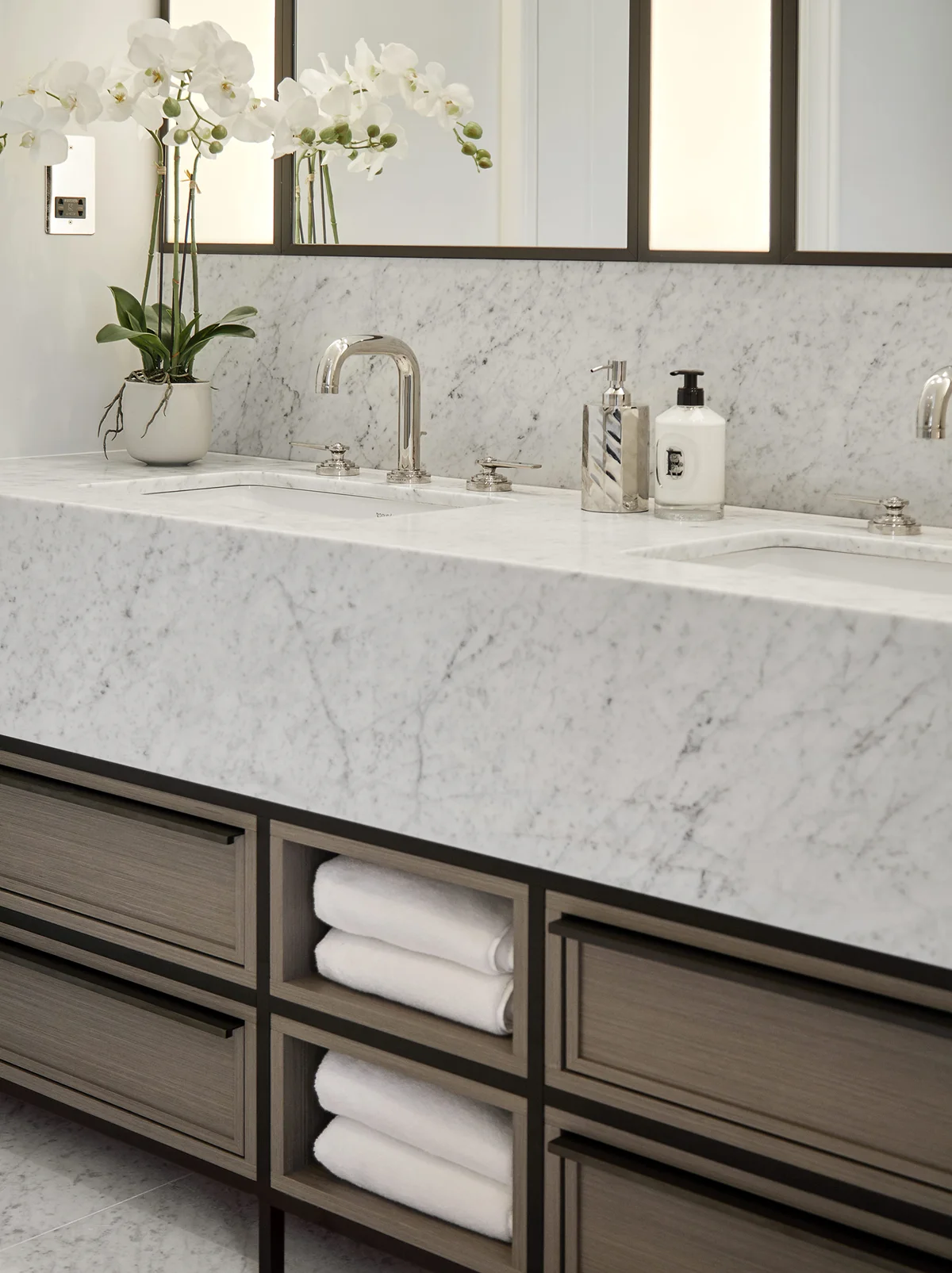 Bathroom vanity with a marble countertop, sink, mirrors, and neatly stacked towels in a cabinet beneath.