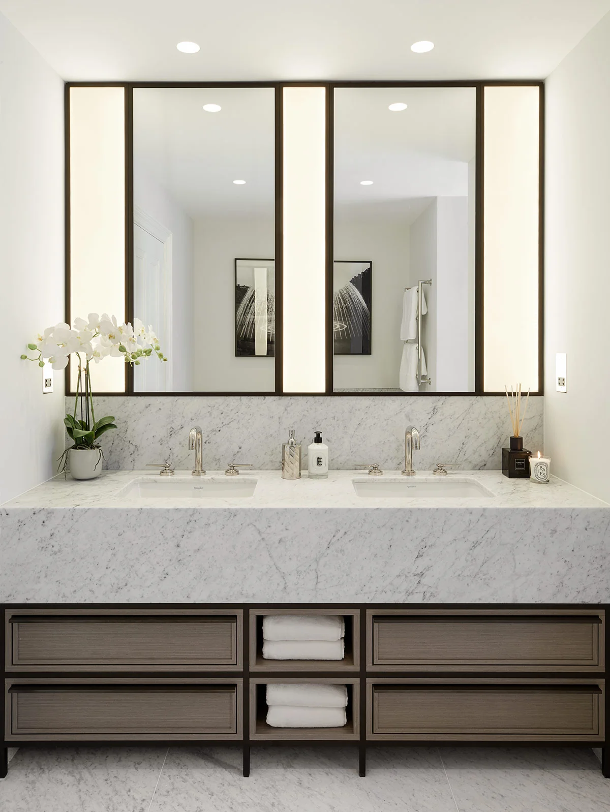 Modern bathroom with double sinks, large mirrors, and marble countertops, featuring stylish storage below and a potted