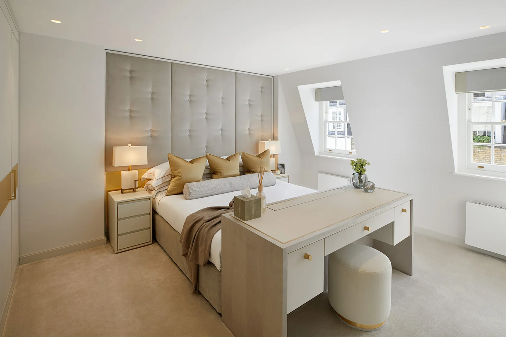 Bright, modern bedroom with neutral tones, plush bedding, bedside lamps, and a stylish desk area.