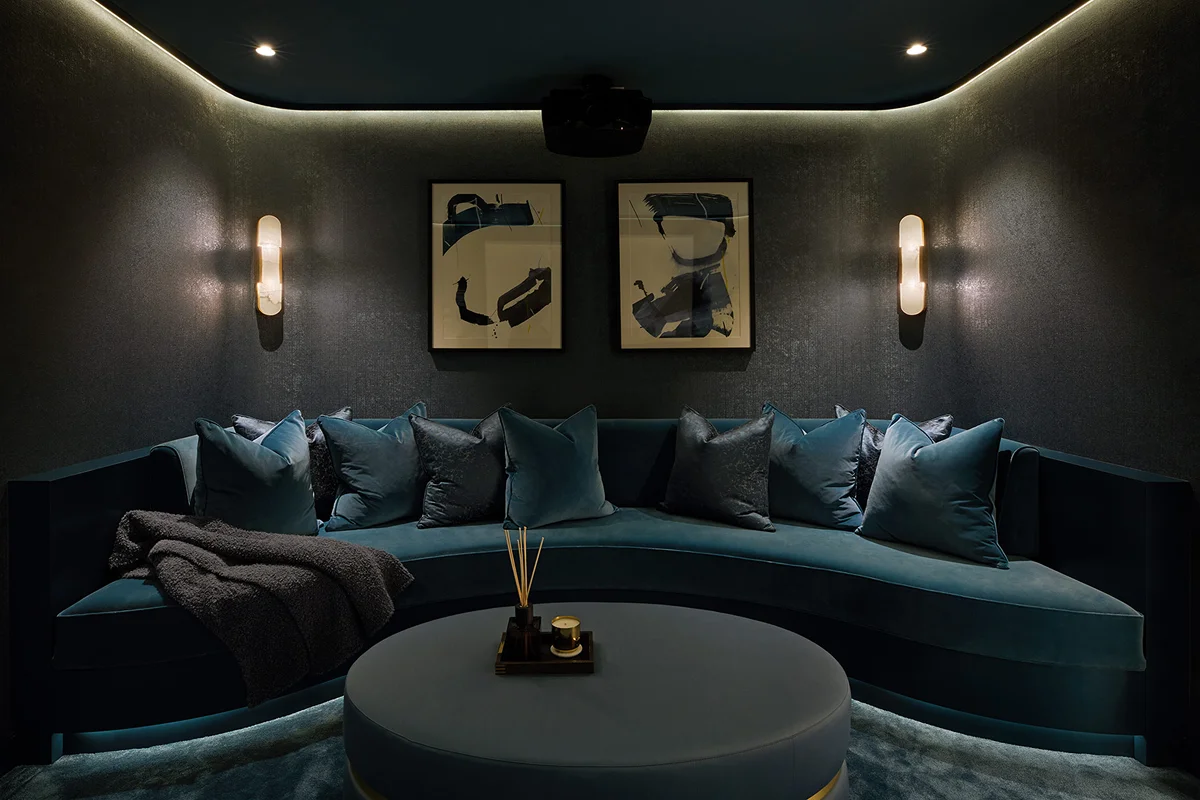 Cozy lounge area with a teal curved sofa, decorative pillows, and two framed artworks on the wall. Soft lighting enhances