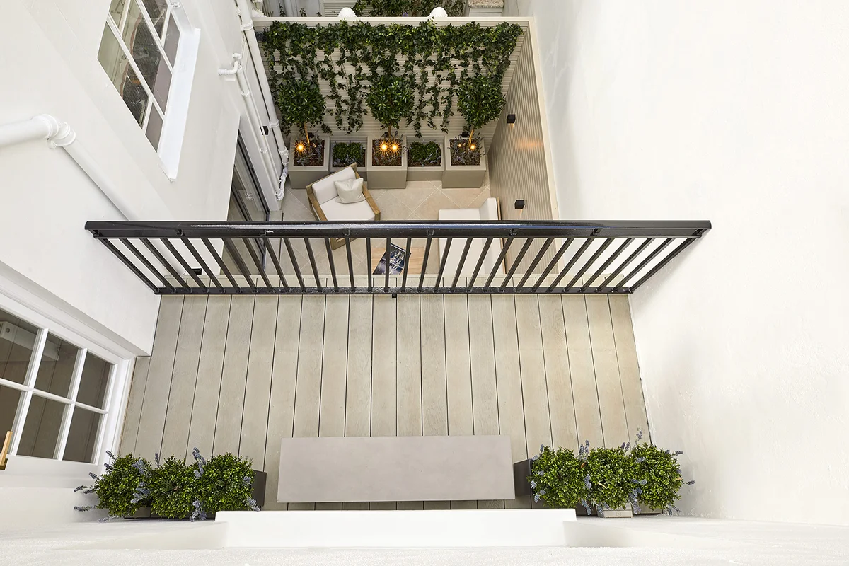 View from above of a balcony with wooden flooring, plants, and a seating area surrounded by green vertical landscaping.