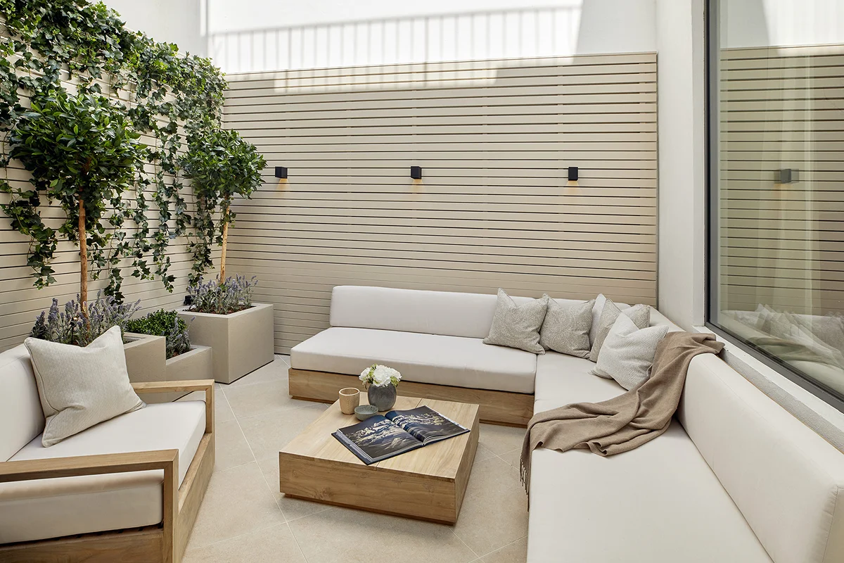 Cozy outdoor seating area with green plants, wooden furniture, and soft cushions in a modern setting.