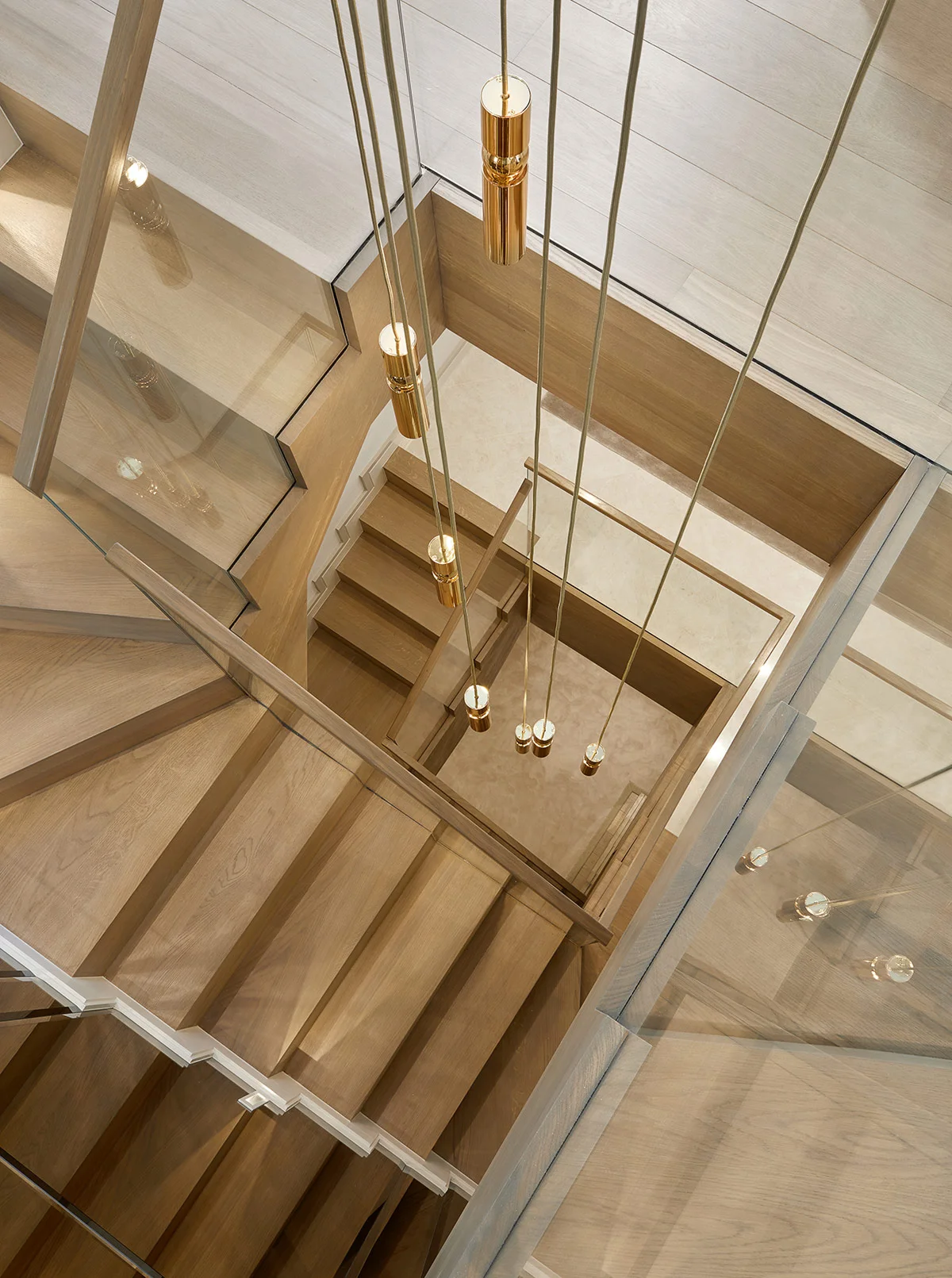 View from above of a wooden staircase illuminated by hanging gold pendant lights, surrounded by glass railings.