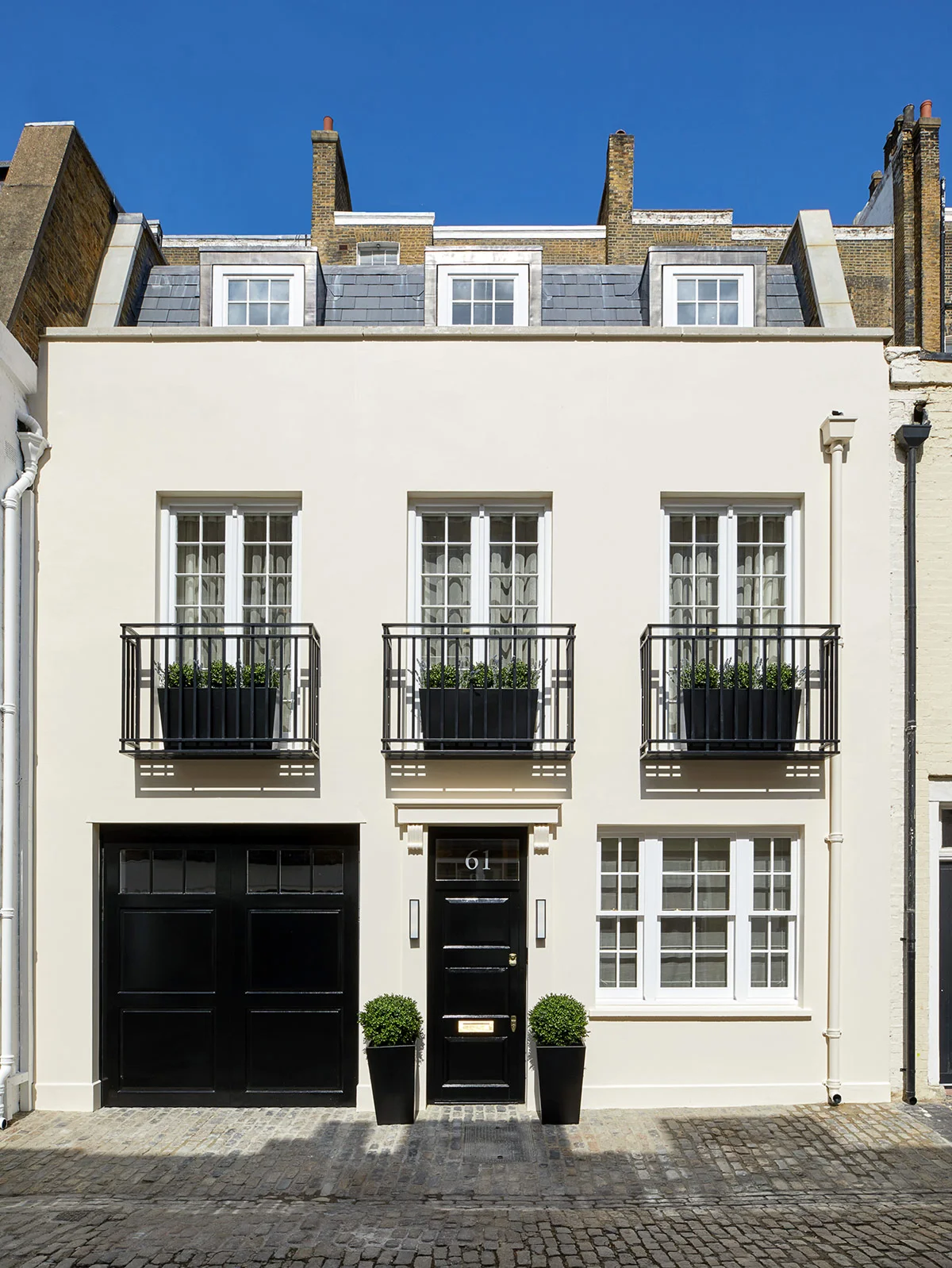 Modern white townhouse with black doors and railings, featuring four windows and two small planters at the entrance.