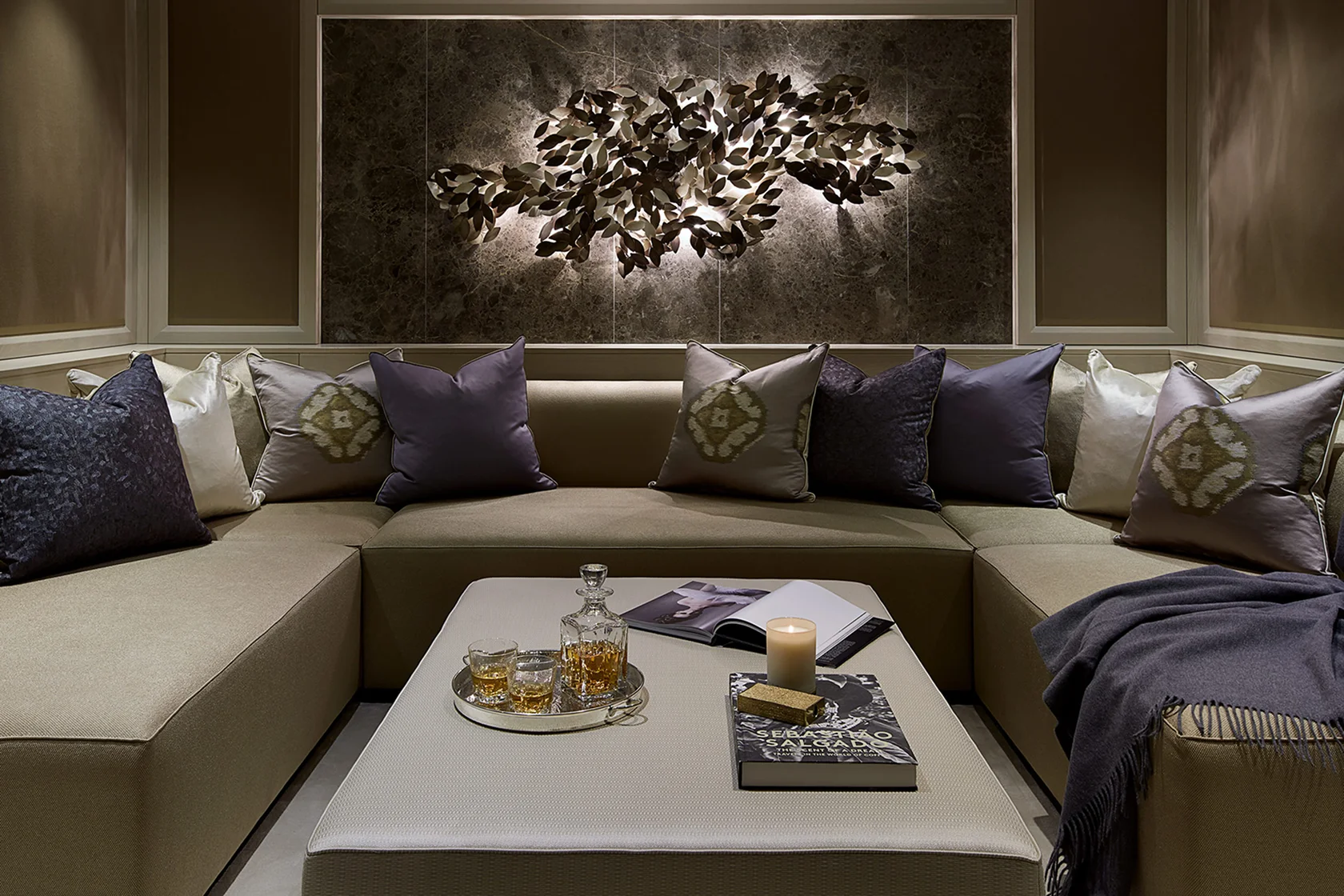 Luxurious living room with a plush sectional sofa, decorative pillows, a coffee table with drinks, and a wall art piece.