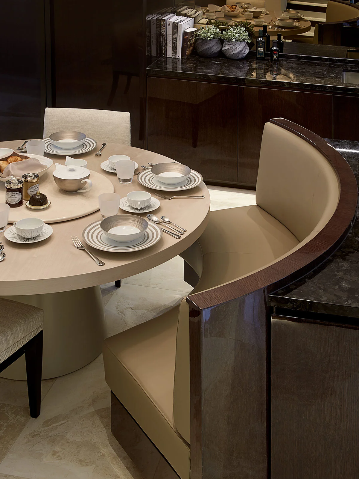 Elegant round dining table set with plates and cutlery, accompanied by modern upholstered chairs in a stylish kitchen.