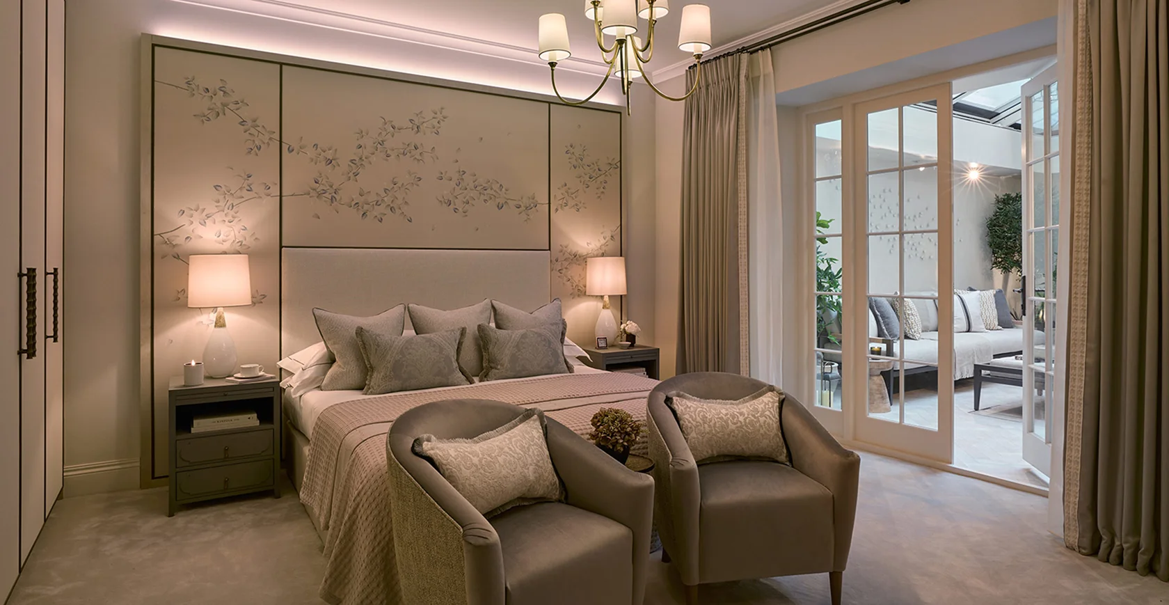Stylish bedroom with a plush bed, armchairs, and a chandelier, featuring soft lighting and elegant decor.