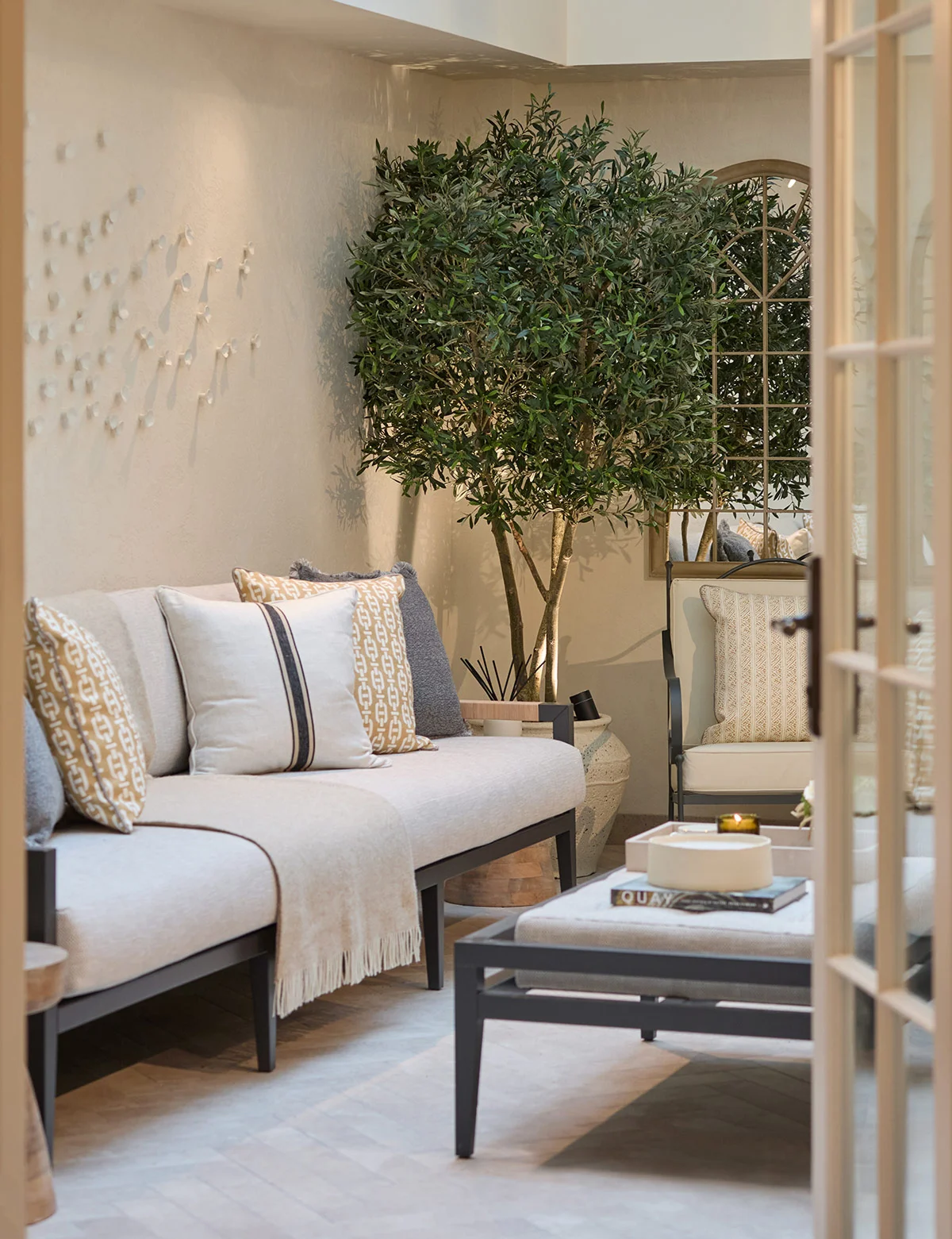 A cozy living area featuring a light sofa, decorative cushions, and a potted tree in a stylish setting.