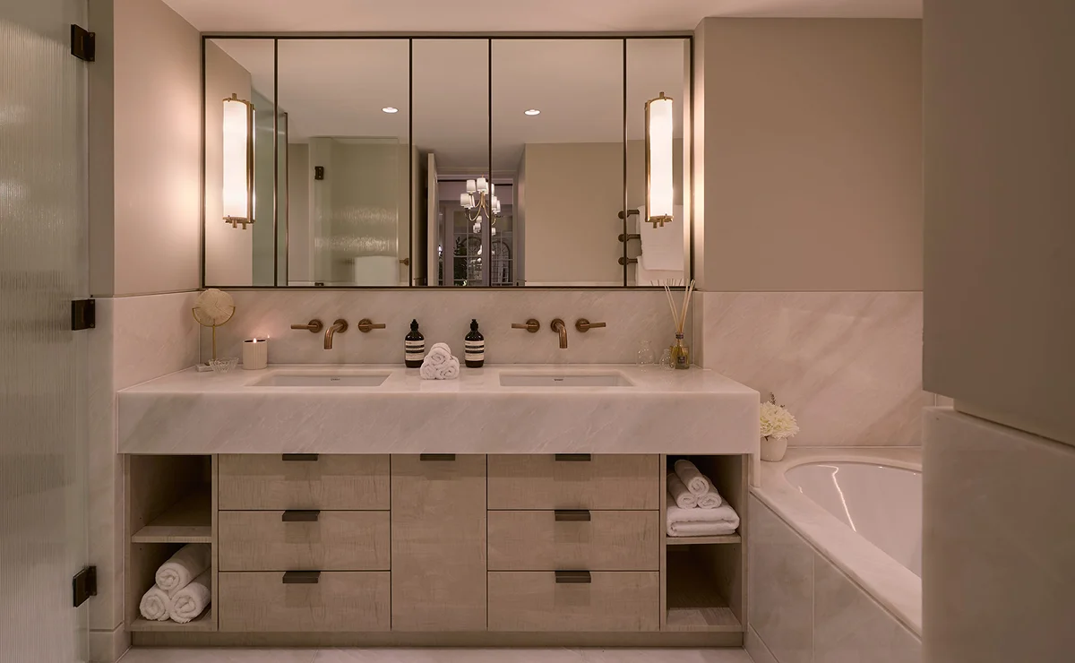 Modern bathroom featuring double sinks, a large mirror, elegant lighting, and a bathtub. Neutral color palette.