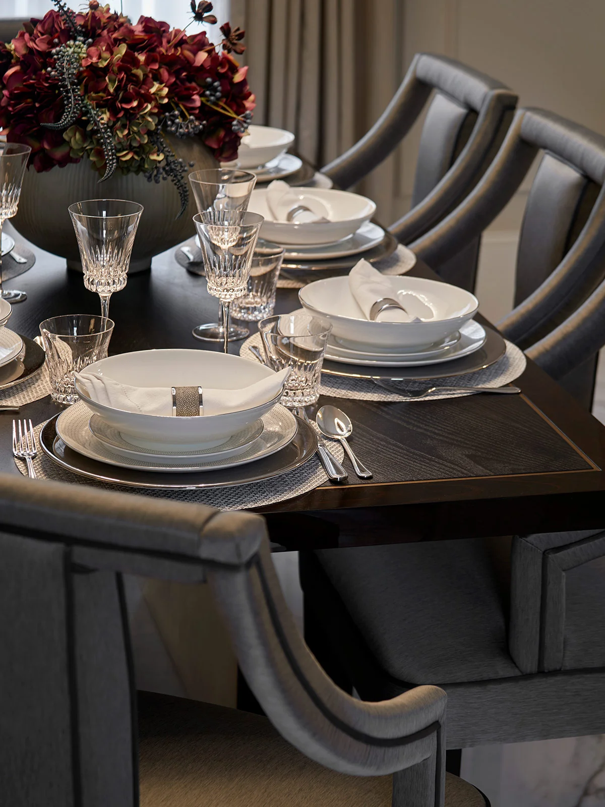 Elegant dining table set with white plates, crystal glasses, and a floral centerpiece.
