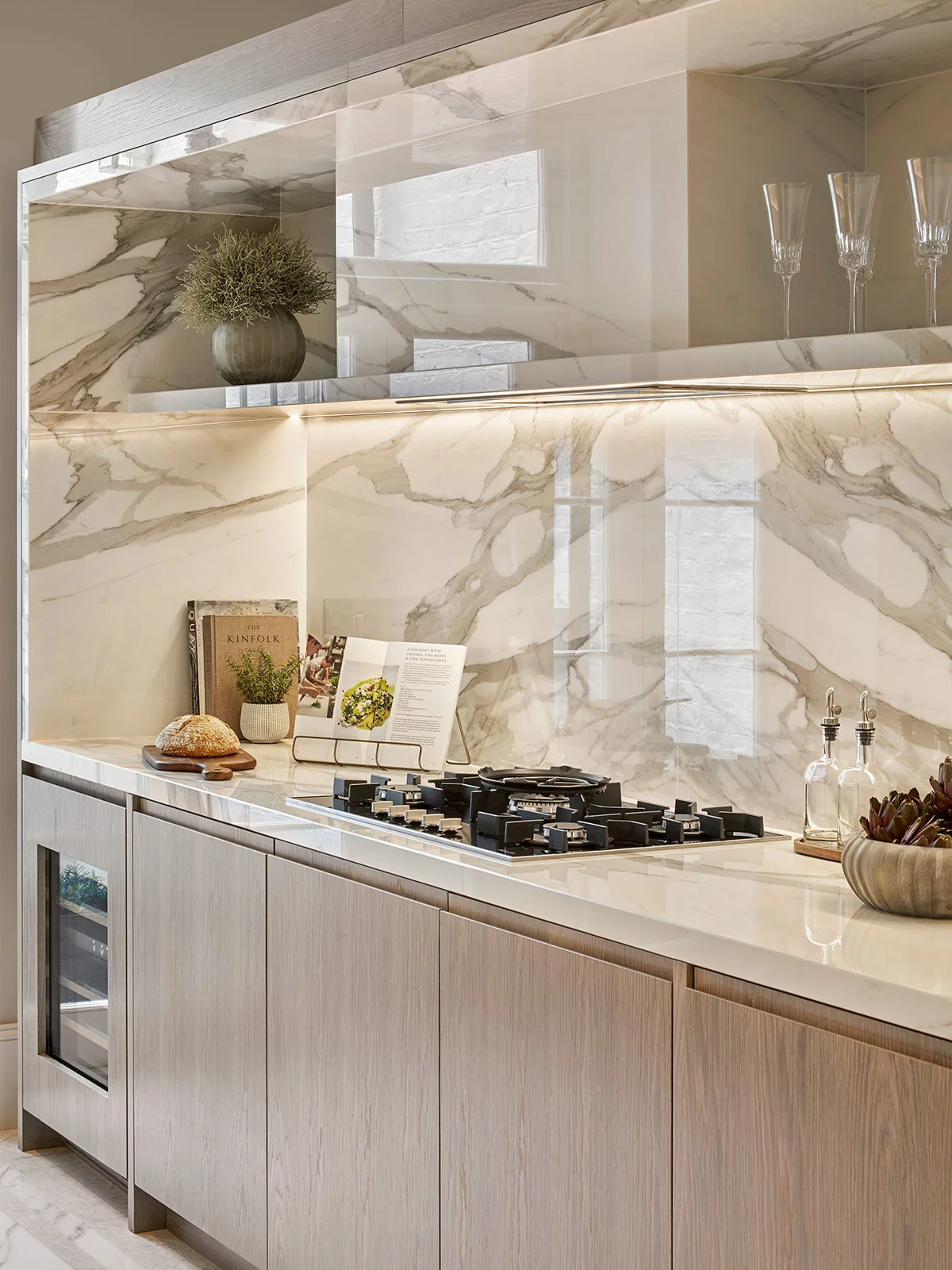 Modern kitchen featuring marble countertops, wooden cabinetry, and a gas cooktop with stylish decor.