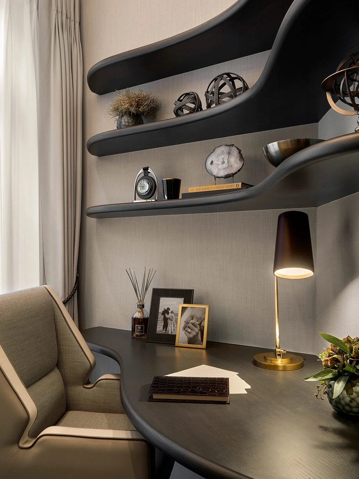 Modern workspace featuring a sleek desk, decorative shelves, lamp, and personal items including a framed photo.