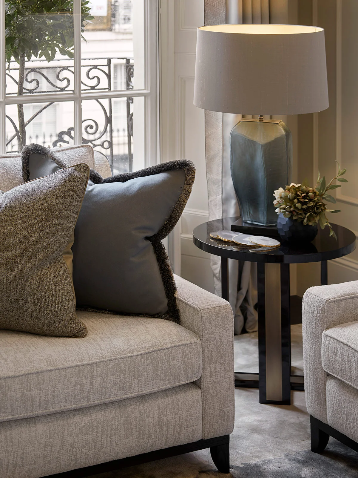 Cozy living room scene with a light gray sofa, decorative pillows, side table, and a lamp casting a warm glow.