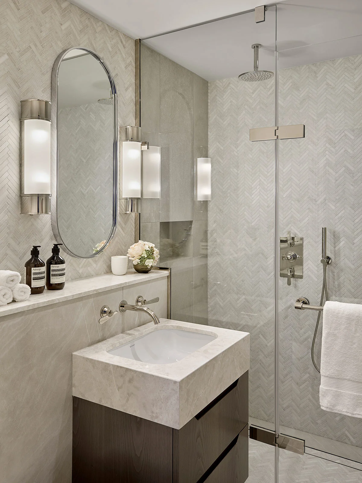 Modern bathroom featuring a sleek sink, stylish mirrors, and a glass shower with elegant lighting.