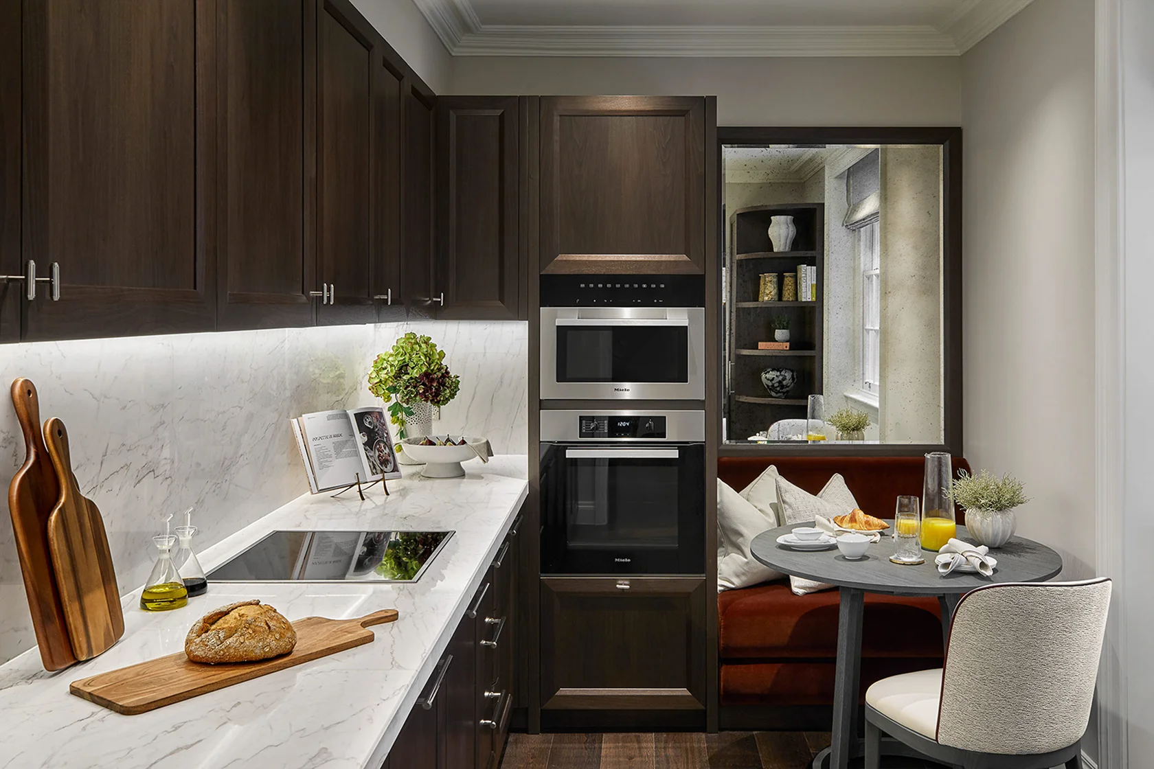 Modern kitchen with dark cabinetry, marble countertops, built-in appliances, and a cozy dining area with a small table.