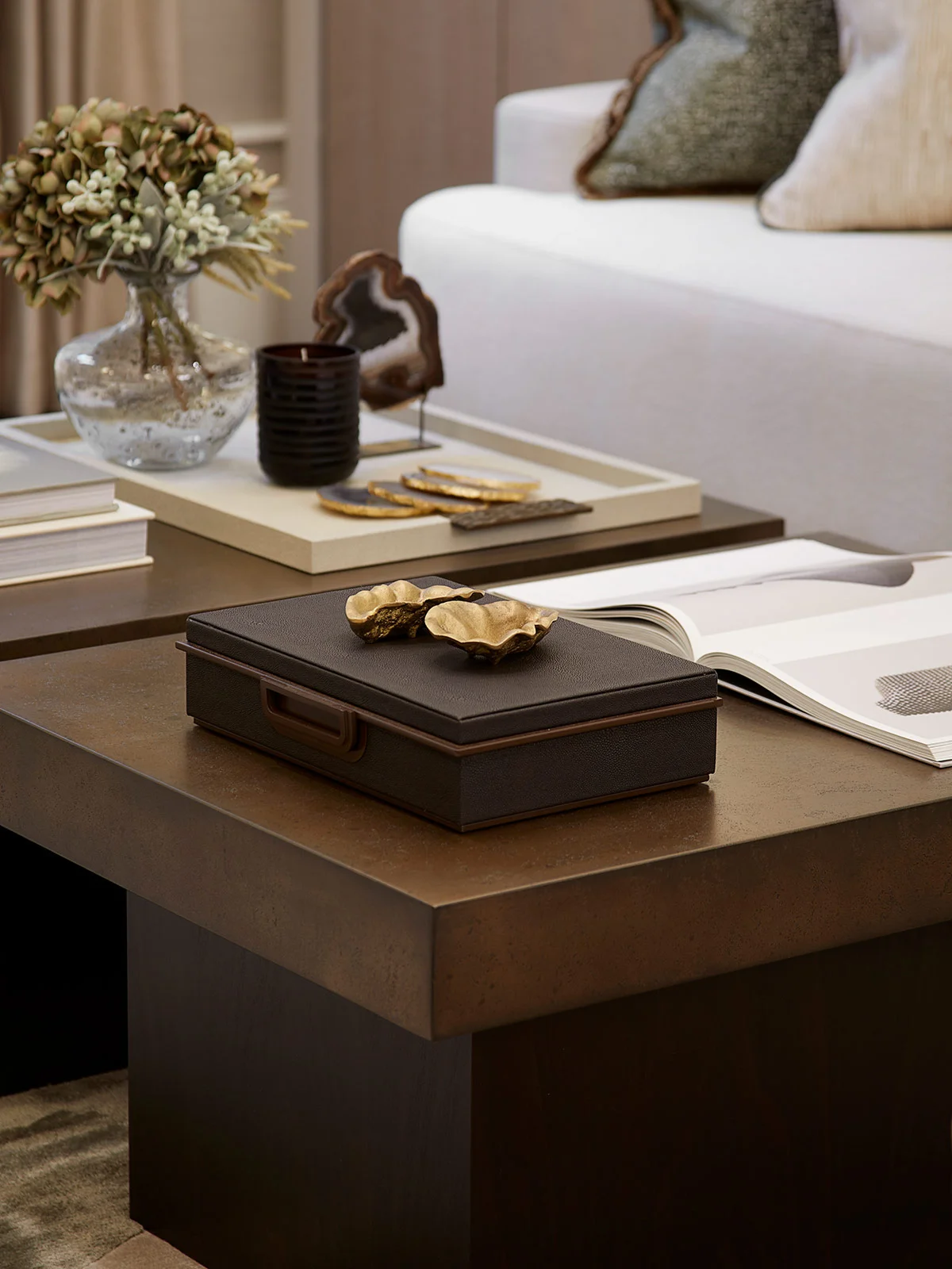 Coffee table with a decorative box, books, a vase of flowers, and a candle, set in a stylish living room.