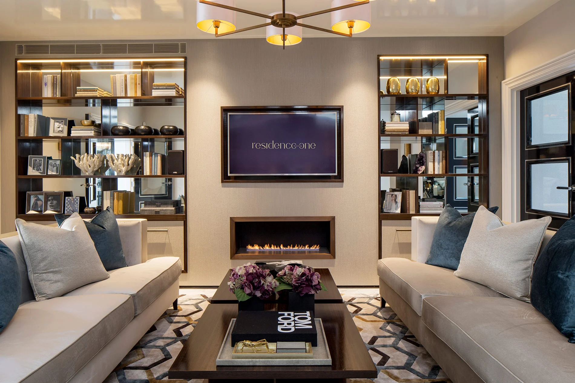 Modern living room with two sofas, decorative shelves, TV, and stylish lighting fixtures.
