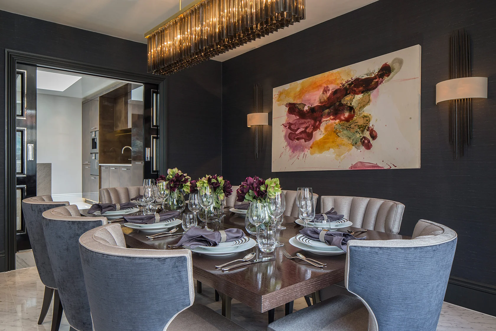 Modern dining room featuring a large round table set with elegant tableware and a colorful abstract painting on the wall.