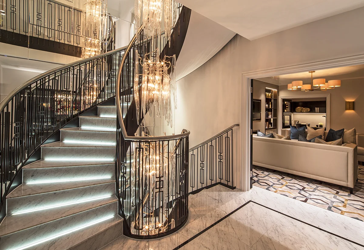 Elegant curved staircase with modern lighting, leading to a cozy living area with stylish furnishings.