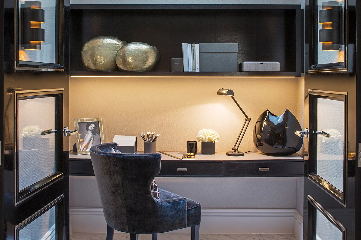 A modern home office with a blue chair, desk, decorative objects, and stylish lighting in a sleek black framework.