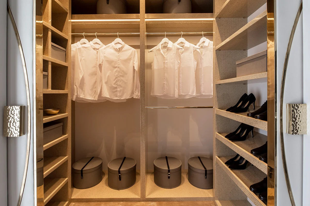 A stylish closet featuring white shirts on hangers, round storage boxes, and shelves with high-heeled shoes.