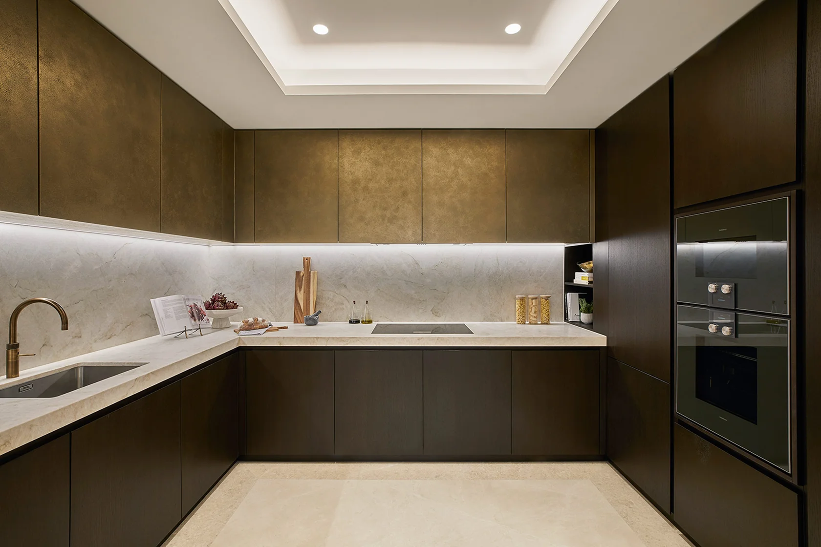 Modern kitchen featuring dark cabinetry, white countertops, a sink, and built-in appliances with soft lighting.