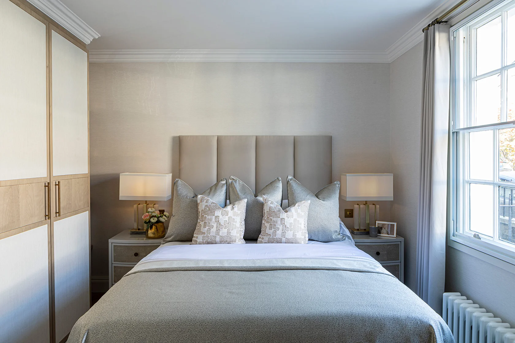 Cozy bedroom featuring a queen-sized bed with decorative pillows, bedside tables, and a window with soft sunlight.