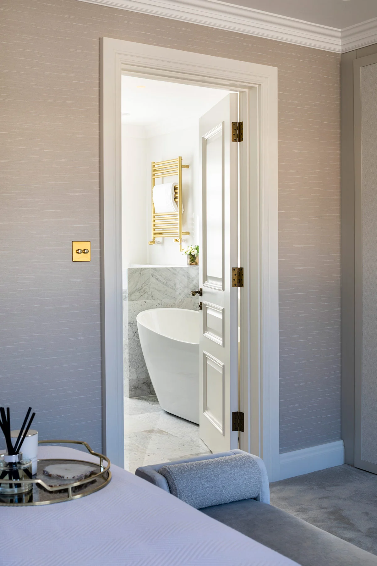 Bright bathroom visible through an open doorway, featuring a freestanding tub and elegant decor.