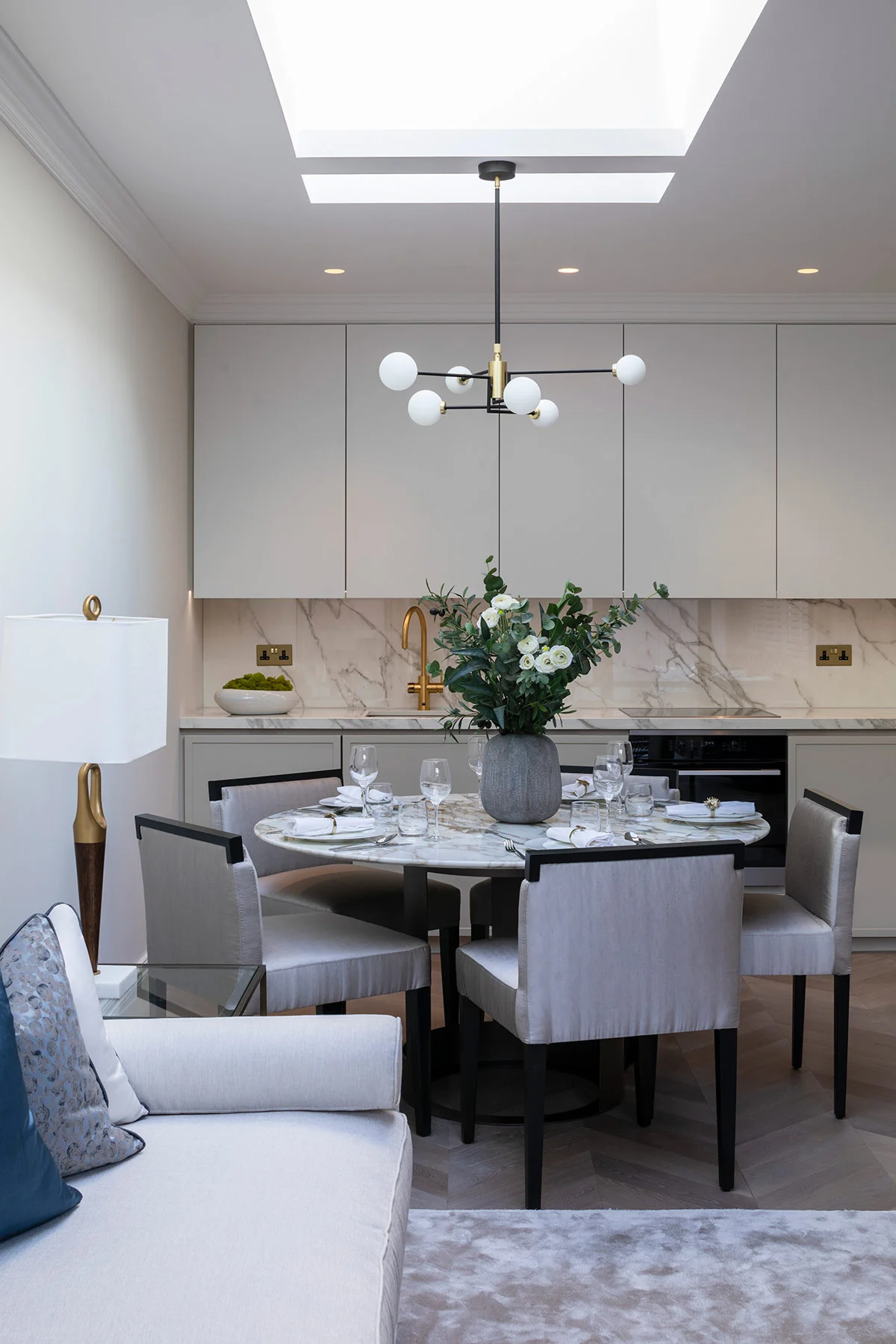 Modern dining area featuring a round table, elegant chairs, a decorative lamp, and a stylish chandelier above.