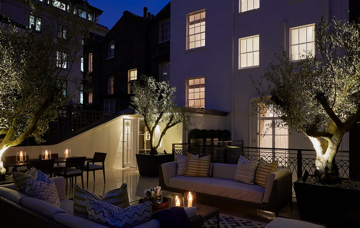 Cozy outdoor lounge with lit trees and candles, featuring a sofa and warm lighting against a night sky.