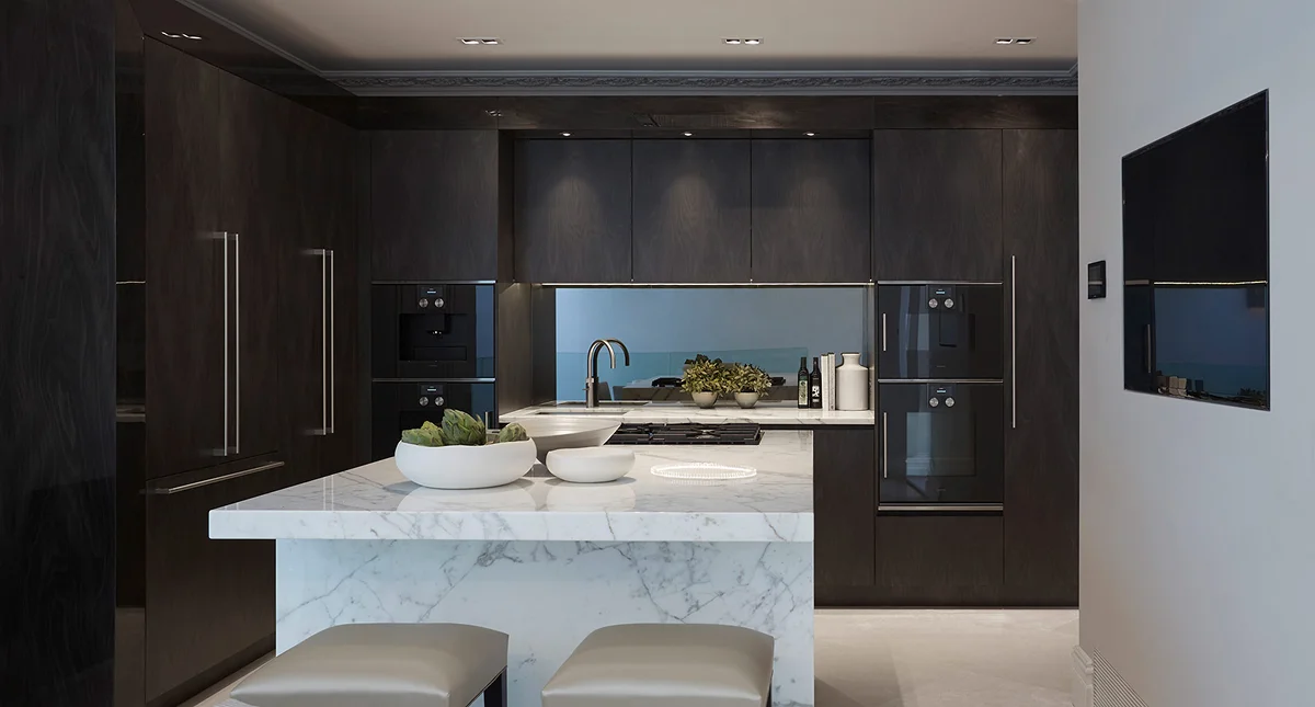 Modern kitchen with dark cabinetry, a marble island, and sleek appliances. Two stools are positioned at the island.